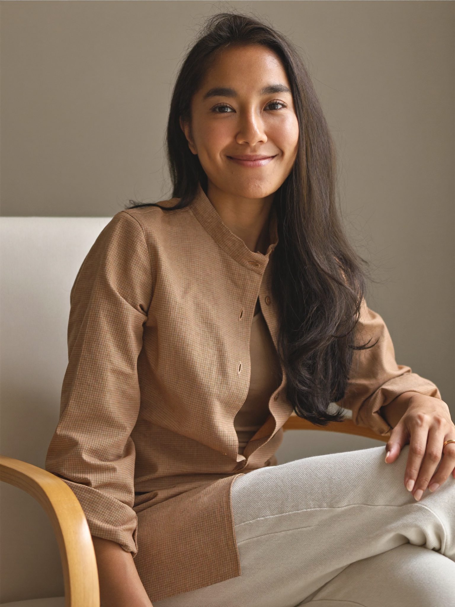Ratih Anjani, pendiri Kainara, berdiri di antara gantungan busana dengan cahaya matahari lembut